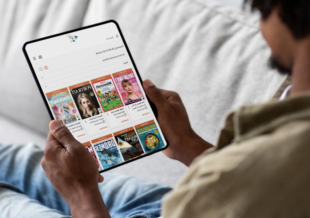 man on a couch holding a tablet and looking at magazines on the Dogwood Library