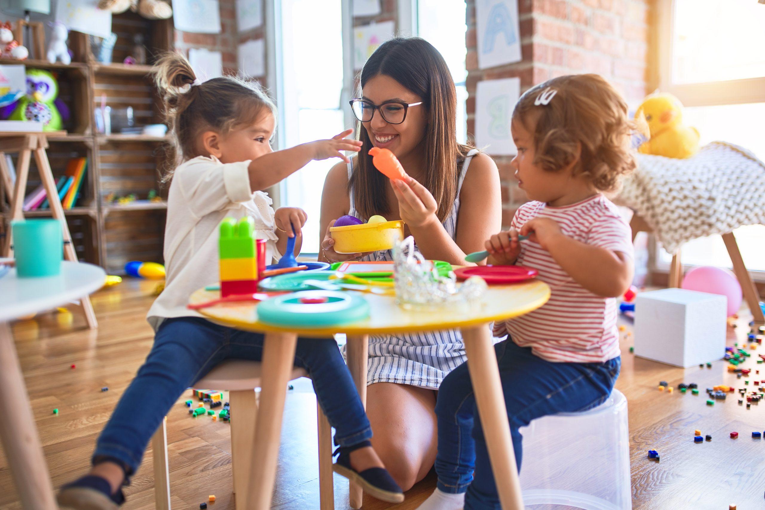 Young teacher and toddlers playing meals using plastic food and cutlery toy at kindergarten